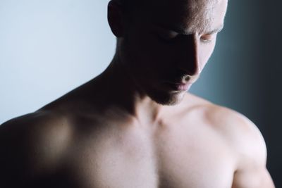 Close-up of shirtless young man standing against wall at home