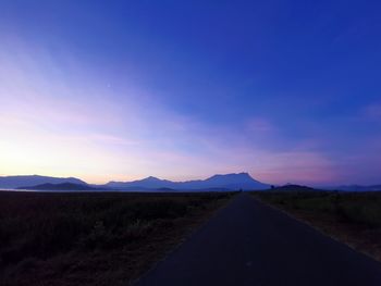 Road leading towards mountains against blue sky