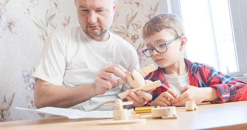 Father and son assembling wooden airplane toy at home