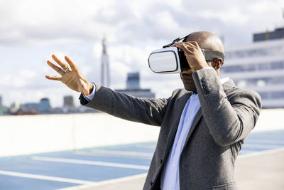 Businessman gesturing while holding virtual reality headset at terrace parking during sunny day