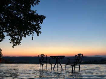 Silhouette trees by lake against clear sky during sunset