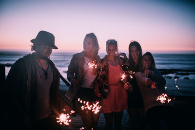 People standing at beach against sky during sunset