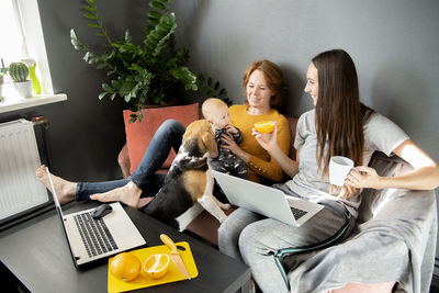 Happy family - grandmother, daughter, newborn baby and dog rest in the living room on the couch