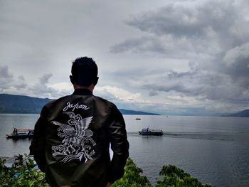 Rear view of man looking at sea against sky