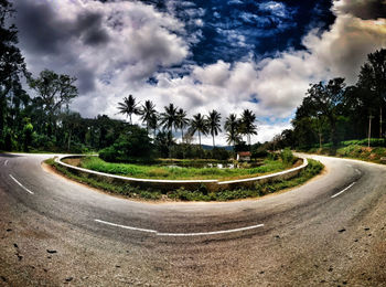 Empty country road along landscape and trees against cloudy sky