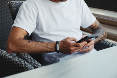Midsection of man using mobile phone while sitting on chair