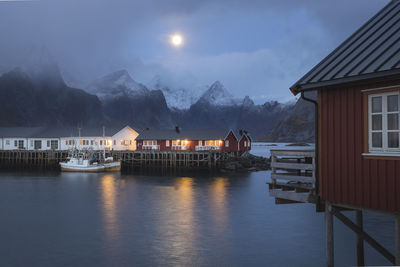 Houses by illuminated buildings against sky