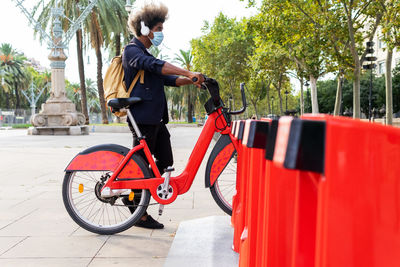 Young black man in a suit and mask listening to music while using a public bicycle on the street