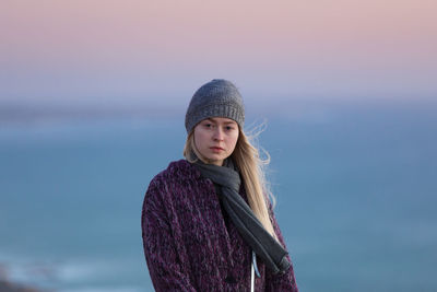 Portrait of young woman standing against sea at sunset