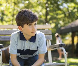 Portrait of handsome caucasian teenage child boy sitting on bench in a park looking away. 