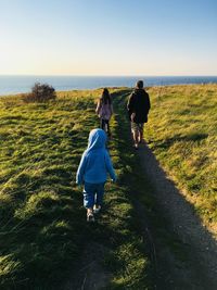 Rear view of family walking on field against sky