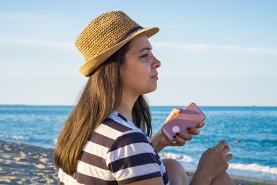 Young woman holding mobile phone and cigarette at beach