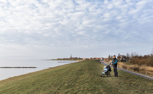 Grandfather standing with granddaughter in stroller at lakeshore