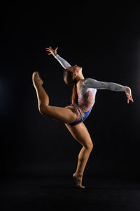 Full length of young woman exercising against black background