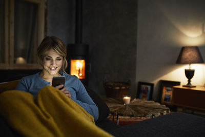 Portrait of smiling woman with smartphone relaxing on couch in the evening
