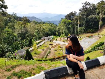 Young woman sitting on tree against mountains