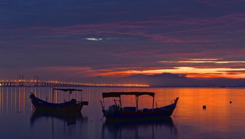 Boats moored in sea against sky during sunset