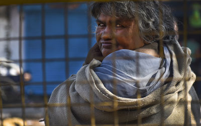 Portrait of senior woman looking over shoulder through metal fence