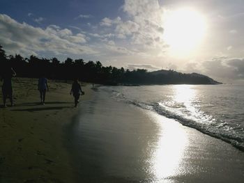 Rear view of people walking on beach against sky during sunset