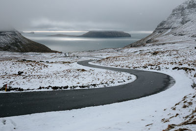 Scenic view of sea by mountains against sky during winter