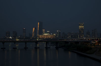 Bridge over river by city against sky at night