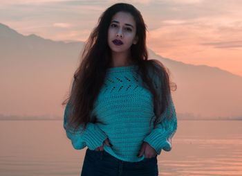 Portrait of beautiful young woman standing against sky during sunset