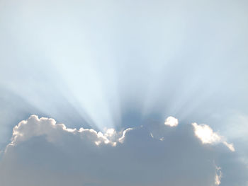 Low angle view of sunlight streaming through clouds