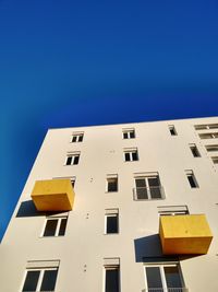 Low angle view of building with yellow balconys against clear blue sky