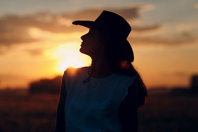 Rear view of woman standing against sky during sunset