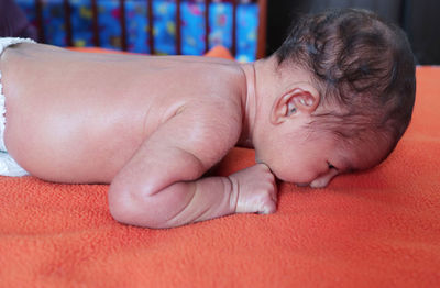 Side view of shirtless baby boy lying on bed