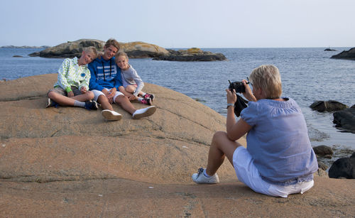 Mother photographing kids at sea shore against sky