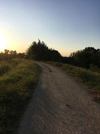 Road amidst field against clear sky during sunset