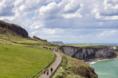High angle view of people walking on cliff by sea against cloudy sky