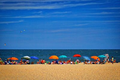 Panoramic view of people at beach against blue sky