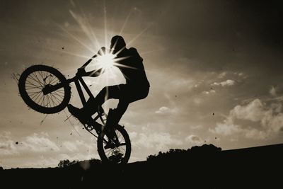 Low angle view of man performing stunt with bicycle against sky during sunset