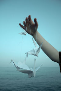 Cropped hand of young woman holding paper cranes against sea
