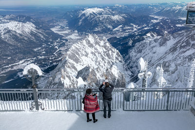 Rear view of people standing by railing on snow