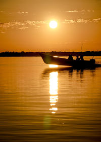 Silhouette people on lake against sky during sunset