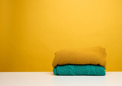 Stack of washed folded clothes on a white table, yellow background. routine homework, copy space