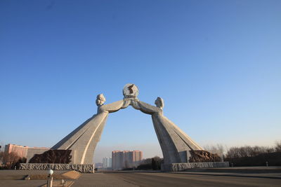 Low angle view of statues over road against clear blue sky