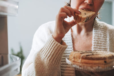 Attractive friendly brunette woman middle age in cozy cardigan eating cake from refrigerator 