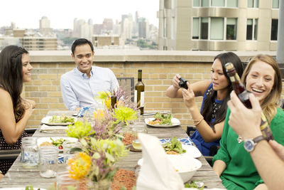 Happy friends enjoying meal on building terrace in city