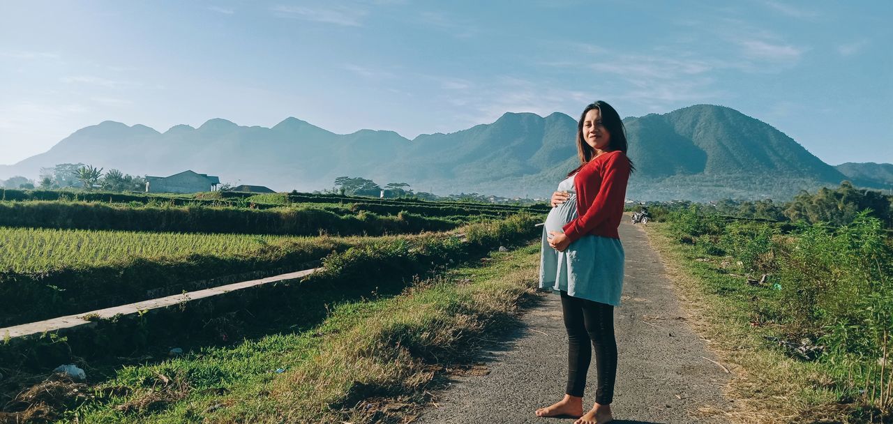 BEAUTIFUL WOMAN STANDING ON MOUNTAIN AGAINST SKY