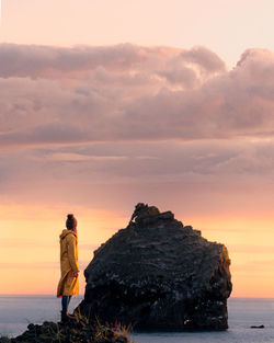 Rear view of women standing at beach against sky during sunset