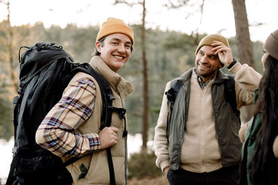 Side view portrait of smiling young man with backpack standing by friends