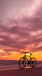 Silhouette man riding bicycle on beach against sky during sunset