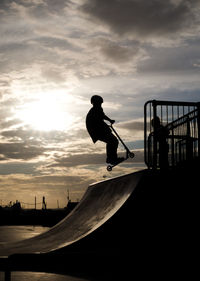 Silhouette boy with push scooter at skateboard park