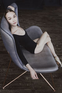 A ballerina in a bodysuit and pointes is sitting on a sofa in a loft with her hands behind her head