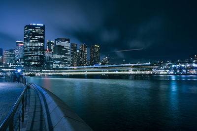 Illuminated bridge over river against buildings at night