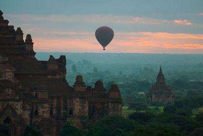 Hot air balloon over temples against cloudy sky at dusk